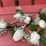Set of five white-rose boutonnieres with baby's breath and twine wrap for the groom and groomsmen.