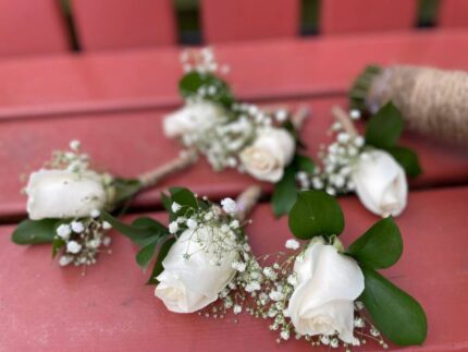 Set of five white-rose boutonnieres with baby's breath and twine wrap for the groom and groomsmen.