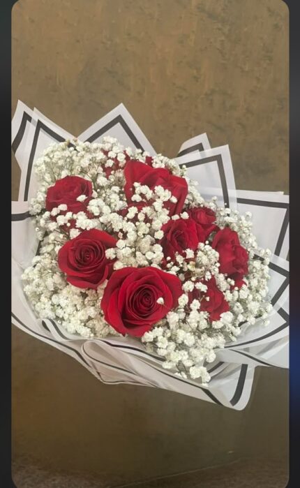 Red roses arranged in a cloud of white baby's breath with geometric white wrapping