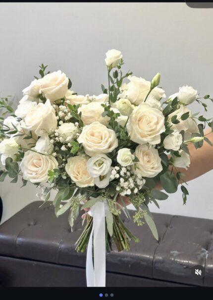 White roses and other white blooms with loose green foliage and trailing ribbon, shown in a supplied reference screenshot.