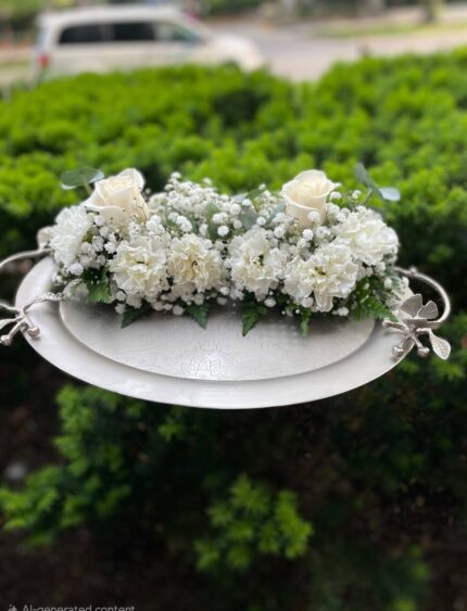 White roses and small white flowers arranged on a silver-tone tray