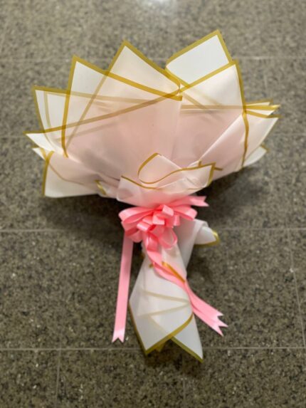 A round cloud of white baby’s breath in blush pink and gold-edged wrapping with a pink bow.