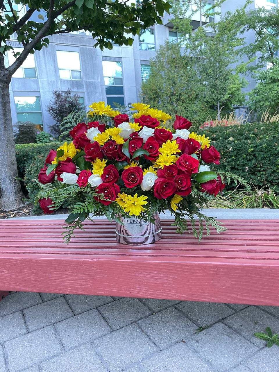 Red roses, yellow daisy-like flowers, white blooms and greenery in a handled basket. Red roses, yellow daisy-like flowers, white blooms and greenery in a handled basket.