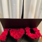 Red roses arranged in letter and heart compartments spelling I love you inside a long dark presentation box.