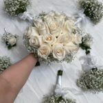 An ivory rose bridal bouquet with coordinating baby’s breath bouquets and white rose boutonnieres.