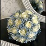 Ivory roses with blue-toned baby’s breath and a rounded silhouette, shown in a supplied reference photograph.