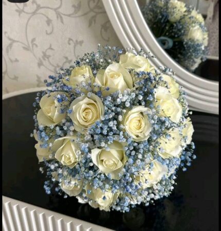 Ivory roses with blue-toned baby’s breath and a rounded silhouette, shown in a supplied reference photograph.