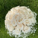 A full rounded dome of ivory roses with discreet white floral accents and a wrapped handle.