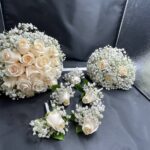 Coordinating ivory rose and baby’s breath bouquets with white rose boutonnieres, photographed in several wedding-group combinations.