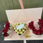 Red roses, wrapped chocolates and a banknote presentation arranged inside a pale pink letter-style gift box.