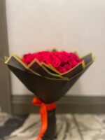 A compact red rose bouquet in black wrapping with gold edges and a red ribbon.