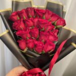 A compact red rose bouquet in black wrapping with gold edges and a red ribbon.