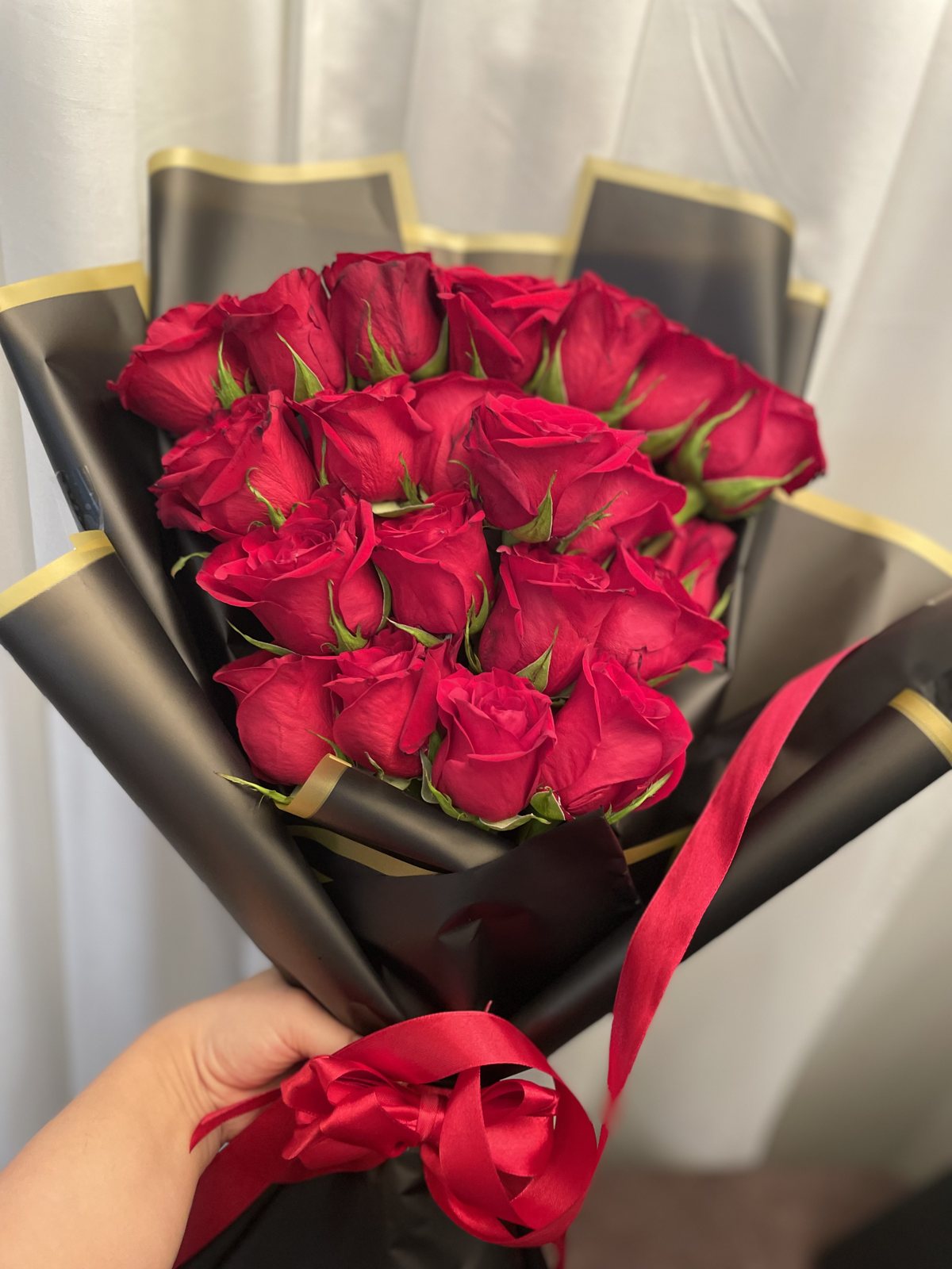 A compact red rose bouquet in black wrapping with gold edges and a red ribbon. A compact red rose bouquet in black wrapping with gold edges and a red ribbon.