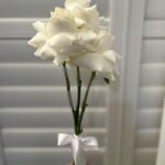 A slender white rose posy with exposed stems and a white bow.