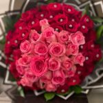 A large red rose bouquet with a pink rose heart, decorative accents and black wrapping.