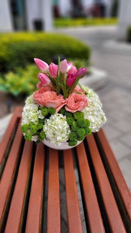 Pink lilies, pink roses, white blooms and green floral accents arranged in a low container.