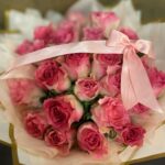 Pink roses gathered in pale gold-edged wrapping and tied with a broad pink ribbon.