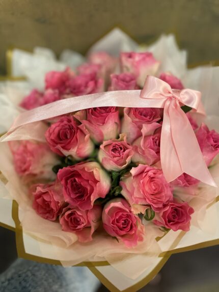 Pink roses gathered in pale gold-edged wrapping and tied with a broad pink ribbon.