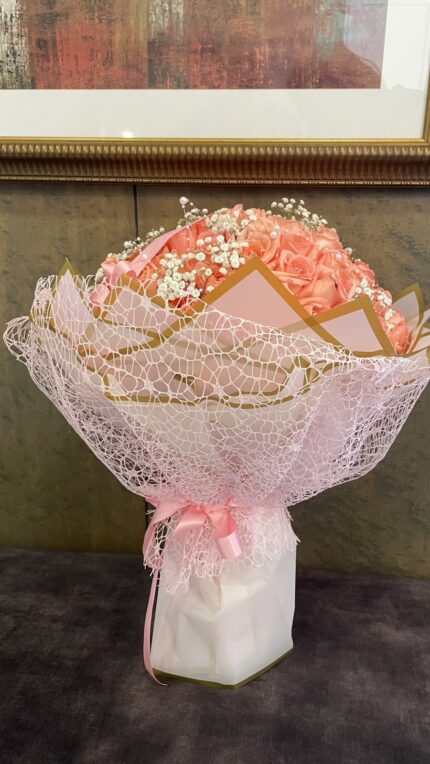 Pink roses with a light baby’s breath accent, pale pink lace-style wrapping and a ribbon finish.
