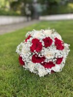 Red and ivory roses woven through white baby’s breath in a rounded bridal bouquet with light ribbon.