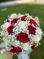 Red and ivory roses woven through white baby’s breath in a rounded bridal bouquet with light ribbon.