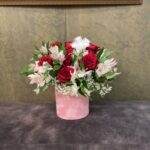Red roses, white flowers, pink alstroemeria and baby’s breath arranged in a pink cylindrical hatbox.