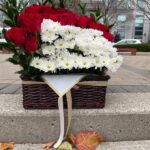 Red roses and a rectangular panel of white daisy-like flowers with foliage in a dark basket.