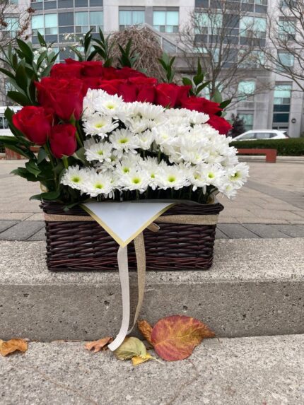 Red roses and a rectangular panel of white daisy-like flowers with foliage in a dark basket.