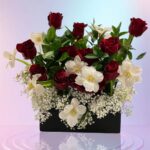 Red roses, white orchid-like blooms, baby’s breath and foliage in a dark box, shown in a supplied reference image.