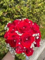 A rounded red rose bridal bouquet with a white baby’s breath edge and light ribbon finish.