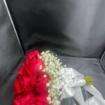A rounded red rose bridal bouquet with a white baby’s breath edge and light ribbon finish.