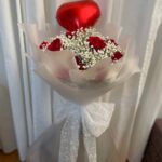 Red roses, baby’s breath and a chocolate accent in white wrapping with a red heart balloon.