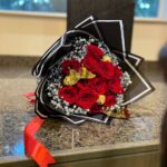 Red roses and gold-wrapped chocolates with baby’s breath and gold butterfly accents in black-and-white wrapping.