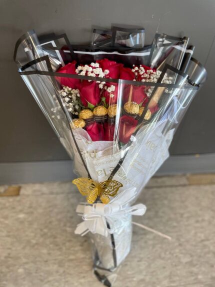 Red roses, white baby’s breath and gold-wrapped chocolates in clear black-edged wrapping with a white bow.