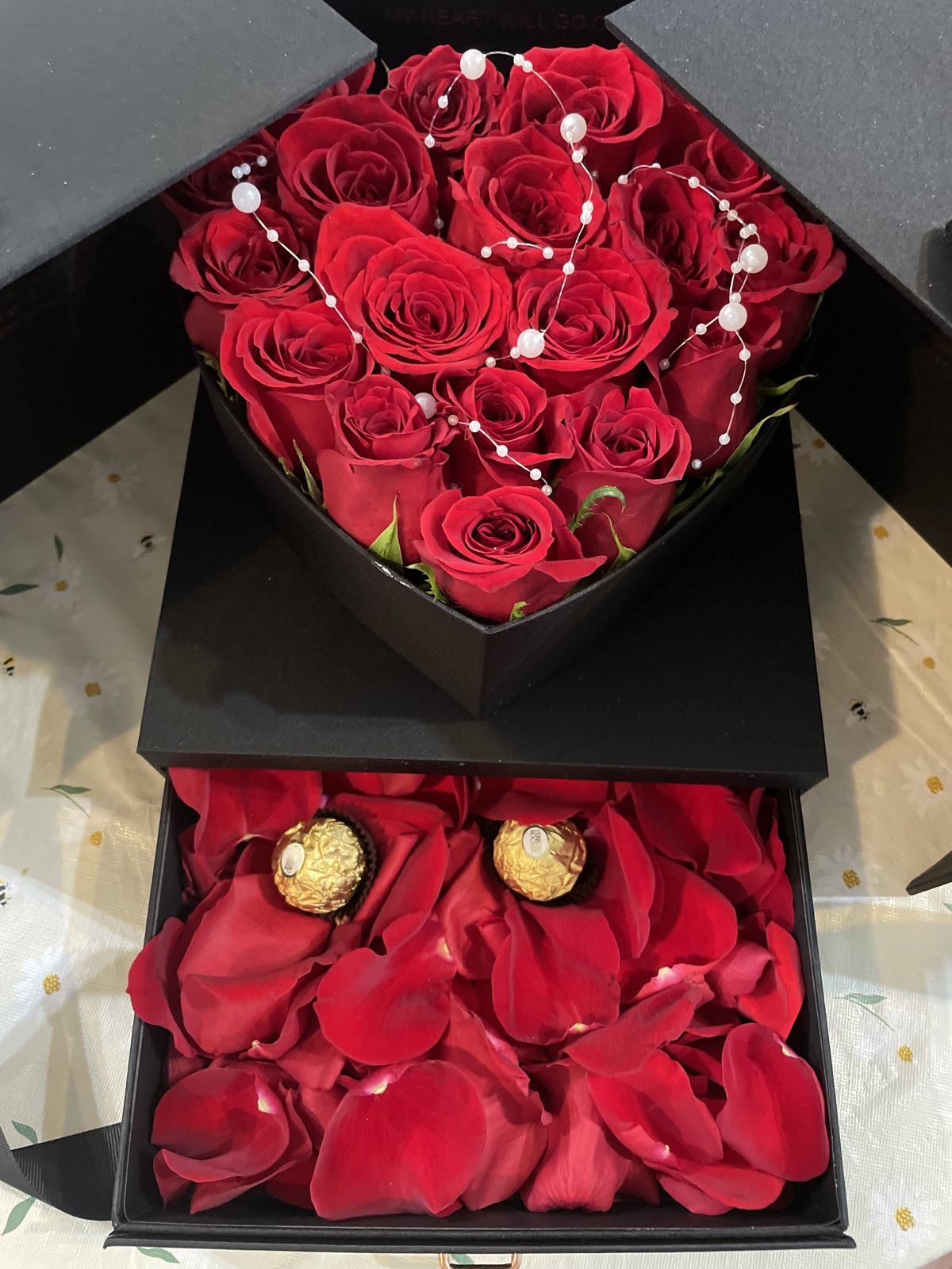 red rose chocolate drawer box Red roses in a black heart-shaped presentation above a drawer with rose petals and wrapped chocolates.