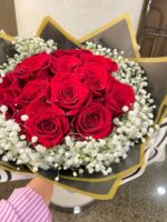 A round red rose centre framed by white baby’s breath and layered gold-edged wrapping.