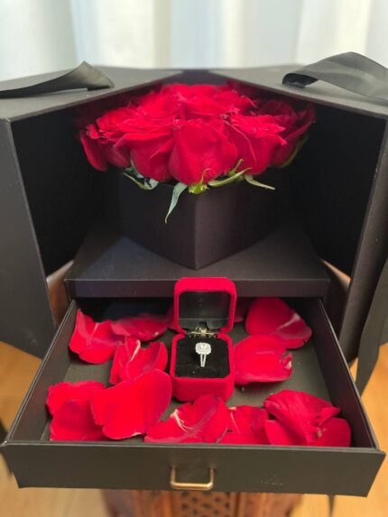 Red roses in a black presentation box with a petal-lined drawer displaying a jewellery case and jewellery.