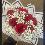Red roses spaced through a white baby’s breath bouquet with angular black-and-white wrapping.