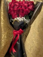 Red roses above a white baby’s breath accent, finished with angular black-and-gold wrapping and a red bow.