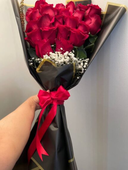 Red roses above a white baby’s breath accent, finished with angular black-and-gold wrapping and a red bow.