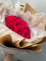 Red roses with small decorative accents in layered printed paper and pale wrapping.
