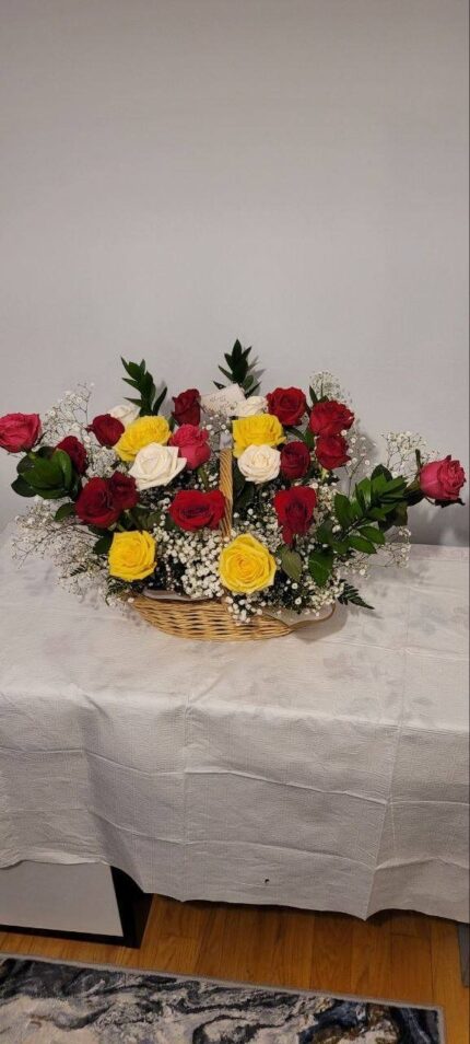 Red, yellow and white roses with other white blooms and green foliage in a low basket.