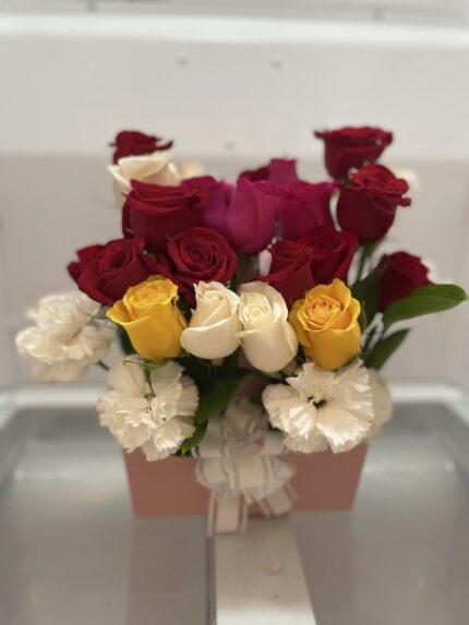 Red, yellow and white roses above ruffled white flowers in a pale pink box.
