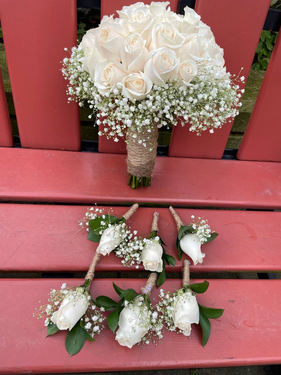 An ivory rose and baby’s breath bridal bouquet with a twine-style handle and coordinating white rose boutonnieres. An ivory rose and baby’s breath bridal bouquet with a twine-style handle and coordinating white rose boutonnieres.