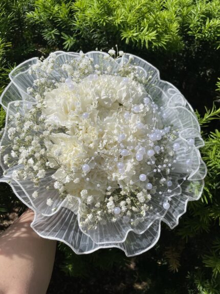White carnations and baby’s breath inside a ruffled translucent collar with decorative white accents.