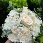 White roses and ruffled white flowers mixed with baby’s breath and eucalyptus-style greenery in a rounded bridal bouquet.