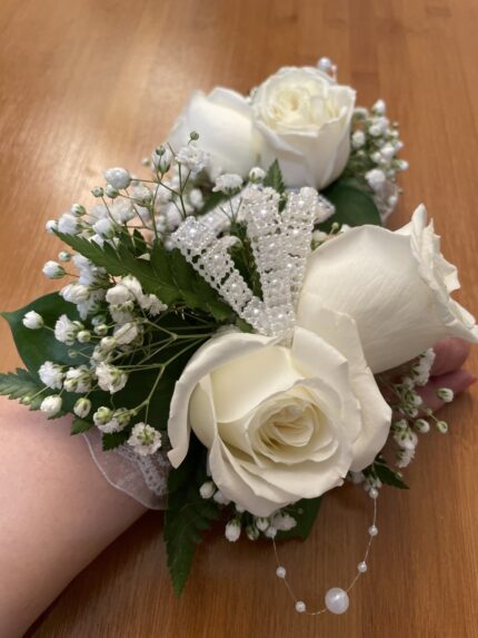 White roses, baby’s breath, green leaves and decorative bead-style sprays in a wrist corsage.