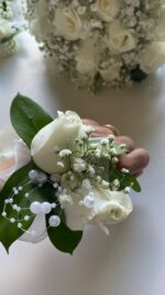 White rose blooms, baby’s breath and green leaves on a decorative pearl-style bracelet.