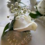 White rose blooms, baby’s breath and green leaves on a decorative pearl-style bracelet.