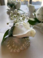 White rose blooms, baby’s breath and green leaves on a decorative pearl-style bracelet.